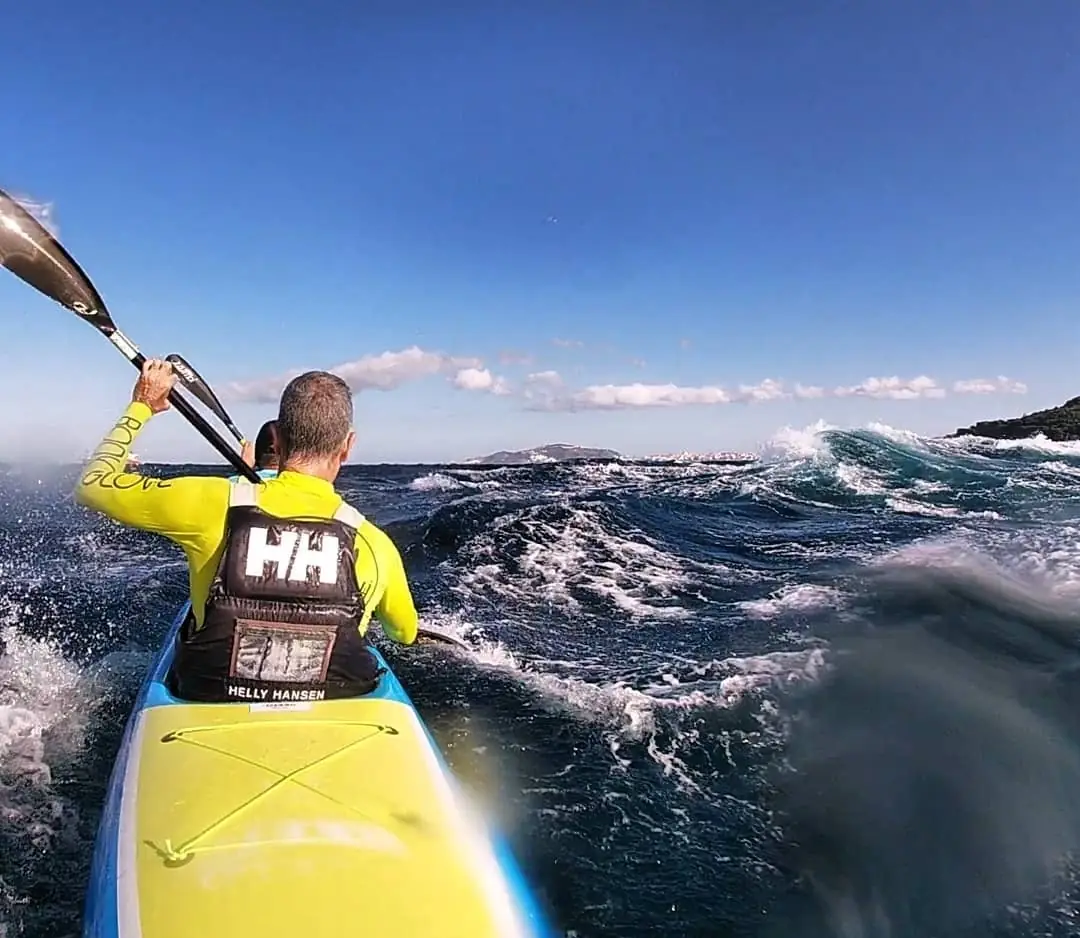 Deportista remando en surfski sobre olas oceánicas frente a la costa